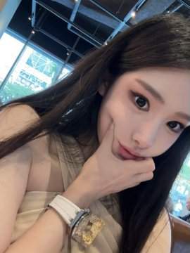 The image features a woman with long brown hair posing for a photo, wearing a white dress or top. She has her hand on her chin and appears to be smiling at the camera. The background of the photo includes a window that allows natural light into the room. There is also an element in the image related to the post: "为了惩罚自己昨天3倍做多Aster 乐音棋塔" which translates to "I am a star".