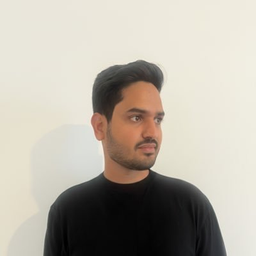 Profile photo of a young man with short dark hair, a beard, wearing a black t-shirt against a plain white wall background.
