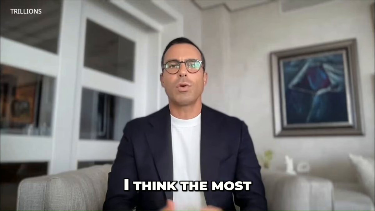 The image shows a man wearing glasses sitting behind a couch with his arms crossed while talking into a microphone, possibly giving a speech or presentation. The text "I Think the Most" appears at the bottom of the image, which could be related to the content being discussed in the scene.