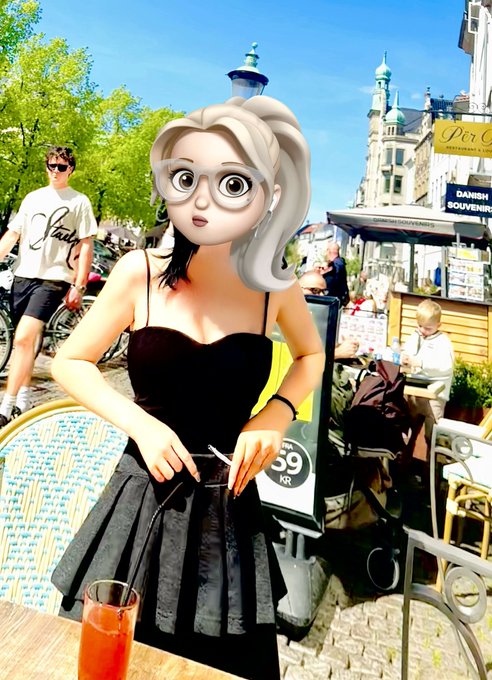 A stylized 3D cartoon character of a woman with white-blonde hair, glasses, and a black dress sits at an outdoor café table with a red drink, set against a real photograph of a European city street scene.