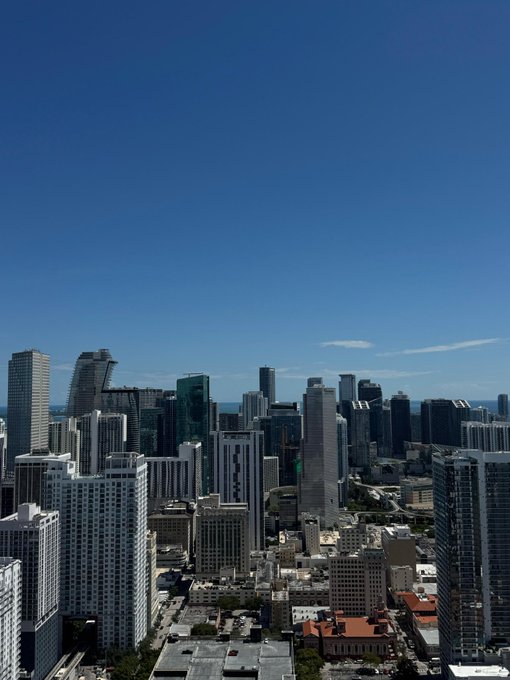 A clear daytime aerial view of a city skyline with high-rise buildings and skyscrapers under a bright blue sky, likely a coastal urban area.
