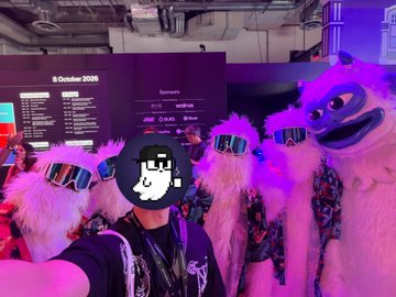 A selfie taken at an event showing a person wearing a pixelated mask and sunglasses, surrounded by people in furry costumes, with an '8 October 2025' schedule visible in the background.
