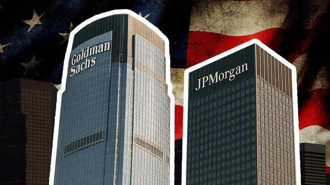 Two skyscrapers displaying the "Goldman Sachs" and "JPMorgan" logos stand prominently against a backdrop of a weathered American flag, visually reinforcing the post's message that major Wall Street institutions like JPMorgan and Goldman Sachs—along with nearly 40 other firms—are actively testing tokenized assets on a blockchain trial overseen by DTCC, signaling traditional finance's deepening move onchain.