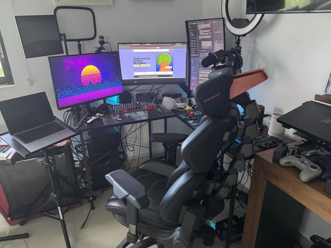 A gaming and streaming setup featuring a COUGAR gaming chair, dual monitors displaying a vibrant retro sunset wallpaper and the text "YOUR DIGITAL SPACE BECOMES REALITY," a vertical screen showing code, an audio mixer, a ring light, and an Xbox controller on a side desk.