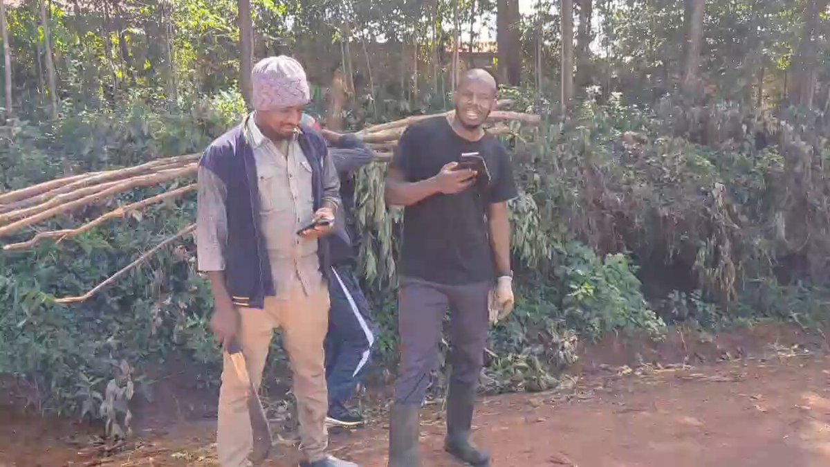 The image shows two men standing next to each other, both holding cell phones. One of them has a backpack with him as well. The man on the left side of the photo appears to be wearing a hat or a scarf, while his companion is not. They seem to be engaged in conversation or possibly discussing something related to their cell phones and the items they are carrying.