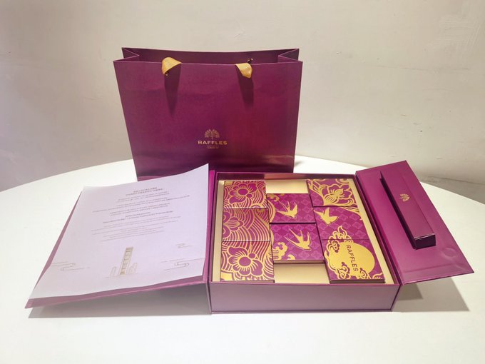 A purple Raffles Singapore gift bag and box set containing decorative pink and gold patterned packages and a certificate of authenticity.