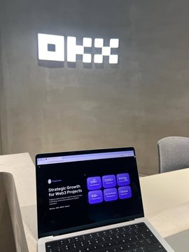 An OKX-branded laptop sits open in front of a glowing OKX sign on the wall, representing the signing of Plagorium's new partnership agreement at the OKX MENA office in Dubai.