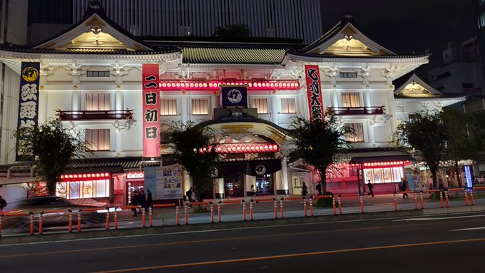 The illuminated Kabukiza theater in Tokyo at night, featuring traditional Japanese architecture with red lanterns and pink banners, one reading '二百回目' (200th time).