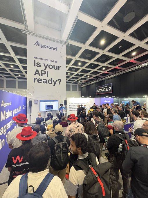 Another angle of the Algorand booth at a conference with a large banner reading 'Agents are paying Is your API ready?' and a crowd gathered around a presentation.