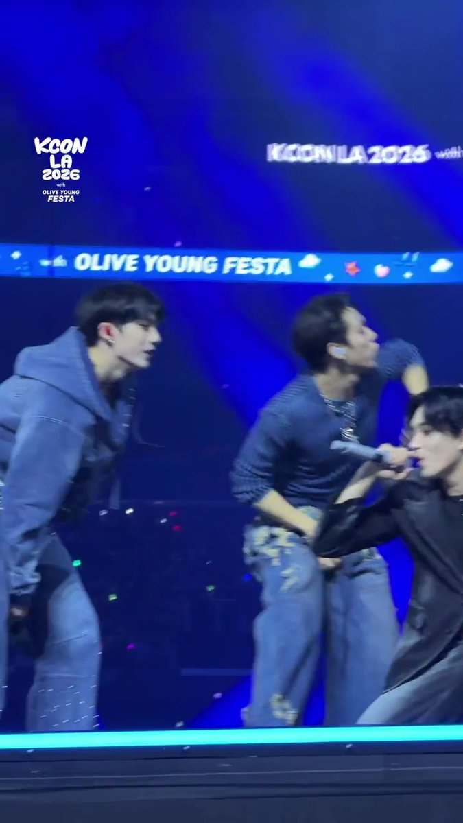 P1Harmony performs on stage at KCON LA 2026's Olive Young Festa on Day 2, with members captured mid-performance against a blue-lit backdrop displaying "KCON LA 2026" and "OLIVE YOUNG FESTA" branding.