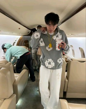 A young man wearing a hoodie with chain prints, baggy pants, and a plush pendant stands in the aisle of a private jet while another person lifts weights in the background, capturing the lavish "crypto king" lifestyle associated with the post's account of allegedly stealing 4,100 BTC through a social engineering scam involving fake exchange security calls.