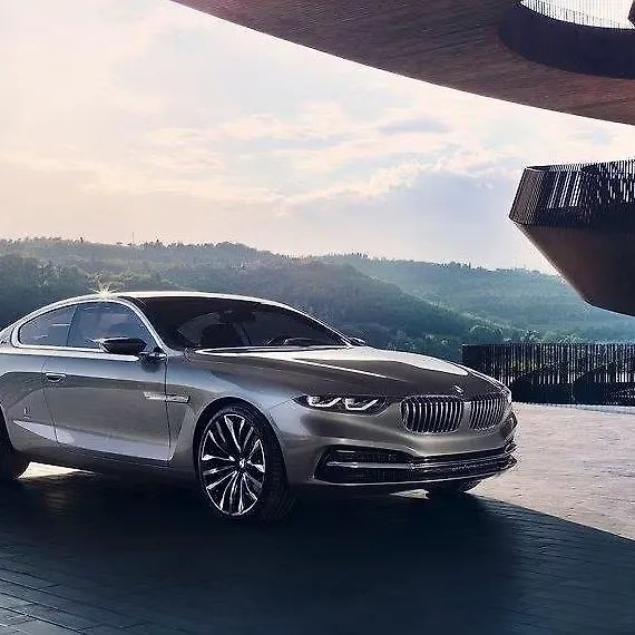 A sleek silver BMW luxury coupe is parked in front of a modern architectural structure with mountain views in the background, embodying the aspirational "Big Win" lifestyle of success and sophistication to start the new week.