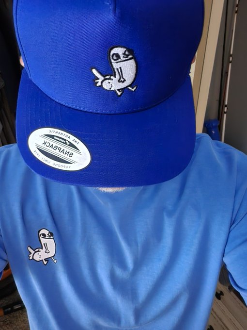 A person wears a blue cap and matching shirt, both featuring the iconic Dickbutt embroidered character, with a Snapback "Yupoong The Ultimate" sticker still on the brim, embodying the poster's "I see dickbutt, I buy dickbutt" motto.