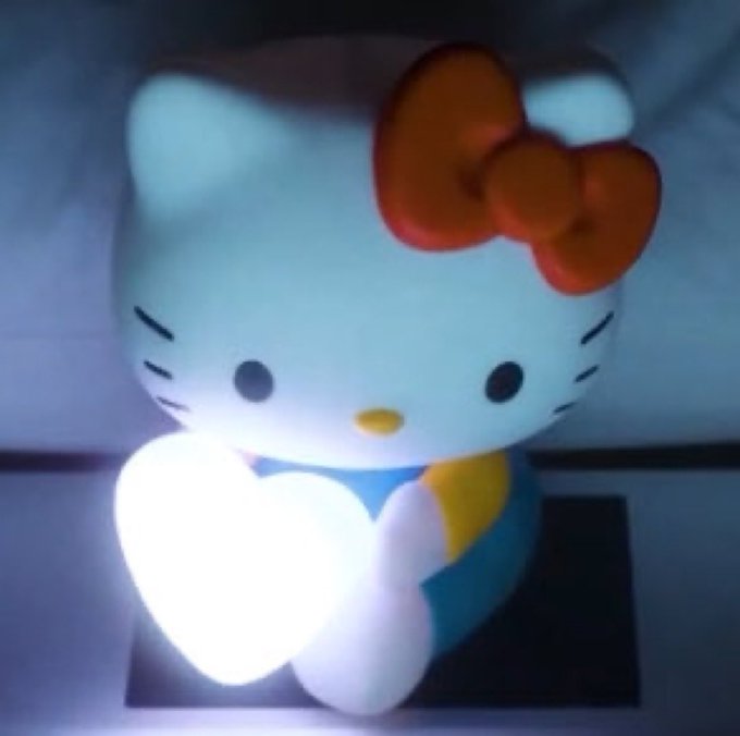 A glowing Hello Kitty figurine holds an illuminated heart-shaped lamp in a dimly lit setting, tying into the $KITTY meme coin's playful branding as the self-proclaimed "greatest cat meme of all time."
