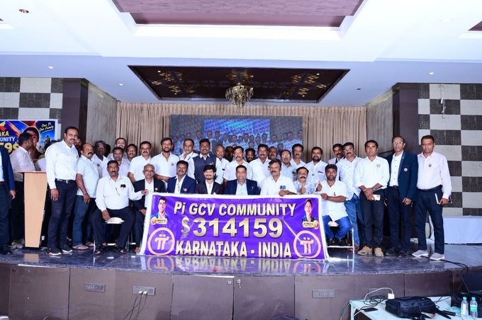 A group photo of men in formal attire posing behind a ceremonial check displaying '$314159' for the Pi GCV Community in Karnataka, India.