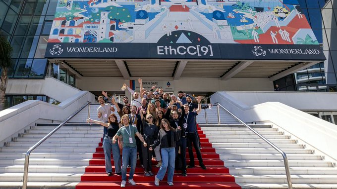 A large group of people posing on a red carpeted staircase at the 'EthCC[9]' conference, held at 'WONDERLAND', featuring colorful decorative artwork above the entrance.