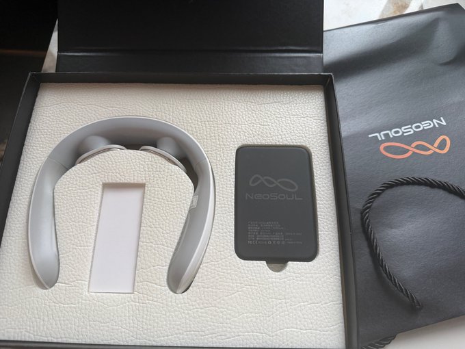 A NeoSoul AI gift box containing a gray neck massager and a black portable charger (power bank) branded with the "NeoSoul" logo, presented in cream-colored packaging with a branded black gift bag beside it.
