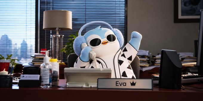 A penguin character wearing sunglasses, fluffy headphones, and a robe sitting at a desk with a nameplate that reads "Eva" while holding a phone receiver and raising a fist.