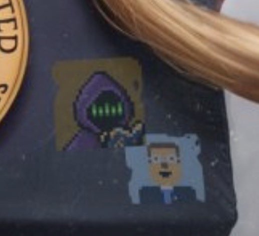 Pixel art stickers featuring a hooded purple character and a small bearded figure displayed on a dark surface.