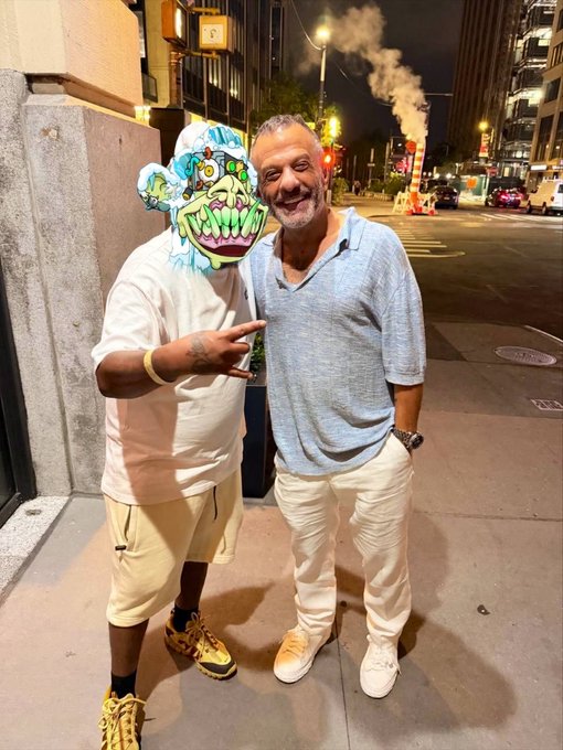 Two smiling men pose on a city sidewalk at night, one wearing a colorful, cartoonish bear mask and making a peace sign, while the other, an older gentleman in a light blue polo and white pants, stands beside him. The caption tags Adam Weitsman as part of the poster's "web 3 Mount Rushmore," highlighting a wholesome encounter at a dinner event hosted by @realstonkbroker.