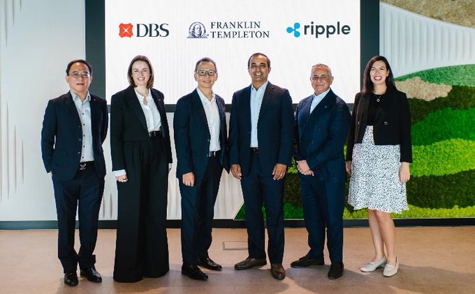 Six executives stand together at a corporate partnership event for DBS, Franklin Templeton, and Ripple, as displayed on the backdrop behind them, representing the firms that collaborated to launch tokenized money market fund (sgBenji) trading and lending solutions on the XRP Ledger using RLUSD stablecoins.