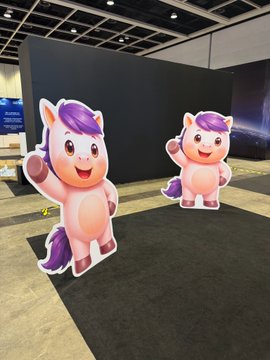 Two identical cardboard cutouts featuring a cute cartoon pink horse/unicorn character with a purple mane, displayed at what appears to be a convention or event.