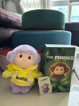 A plush toy wearing a yellow "Solflare" jacket sits next to its "The Monke" branded box and a small tag, with the purple character matching the Superteam-themed "degen monkebubu" mentioned in the post. The collectible's Solflare branding and purple-and-yellow color scheme tie directly to the baby's excitement about the jacket and the Superteam-themed plush.
