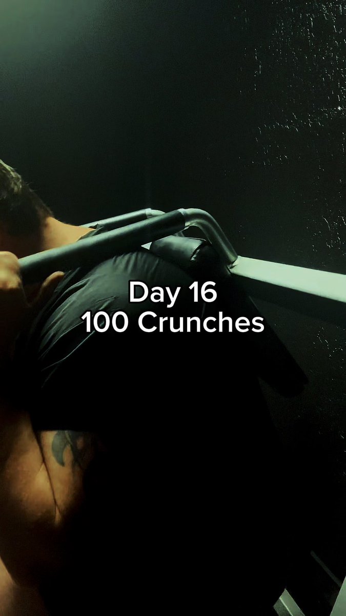 A person performs crunches on an exercise machine in a dimly lit setting, with the text 'Day 16, 100 Crunches' overlaid on the image.