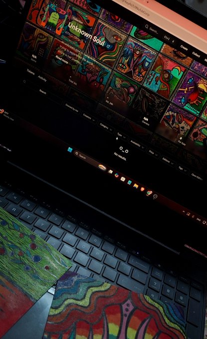A laptop displaying a vibrant digital art portfolio website titled "Unknown Soul," accompanied by colorful painted artwork on the keyboard and desk surface.
