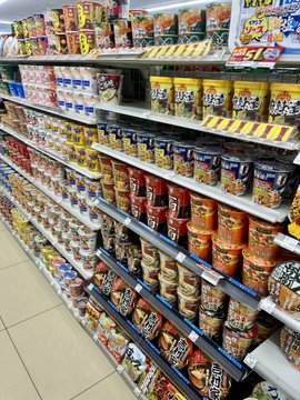 A Lawson convenience store in Minami-Karuizawa displays an impressive Japanese instant noodle selection, prominently featuring large stacks of Cup Noodle containers and various other noodle products lining the shelves, with the post noting the store's surprisingly high-quality selection attributed to its location near the STEPN community.
