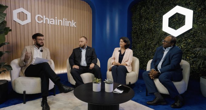 A panel discussion featuring four people seated in white chairs with the "Chainlink" logo displayed on the wall behind them in a blue and green setting.
