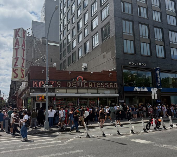 A bustling crowd lines up outside the iconic Katz's Delicatessen in New York City, with visible signage for "KATZ'S DELICATESSEN," "EQUINOX," and "Marshalls" on the surrounding buildings. The image captures the everyday energy of Manhattan street life—an apt parallel to a post noting that "HYPE just hit a new all time high," suggesting that while hype reaches record levels, most people on the street remain oblivious to the market milestone.