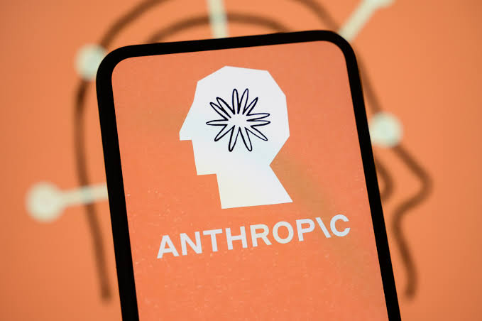 A smartphone displays the Anthropic logo—an "A" formed by a human head profile with a starburst inside—against an orange background featuring circuit board patterns, with the text "ANTHROPIC" beneath it. The image illustrates the post's point about Anthropic moving toward designing its own AI chips rather than relying solely on third-party hardware providers like Nvidia, AMD, Google, and AWS.