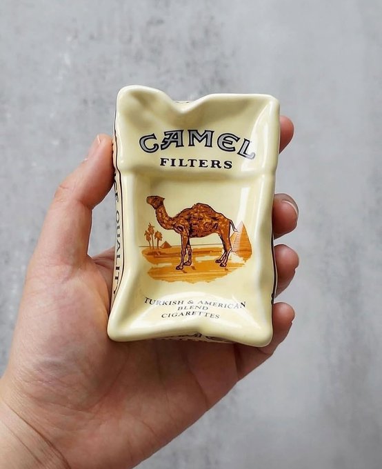 A hand holds a ceramic Camel cigarette pack-shaped container featuring the classic camel and pyramid illustration, labeled "CAMEL FILTERS" and "Turkish & American Blend Cigarettes."