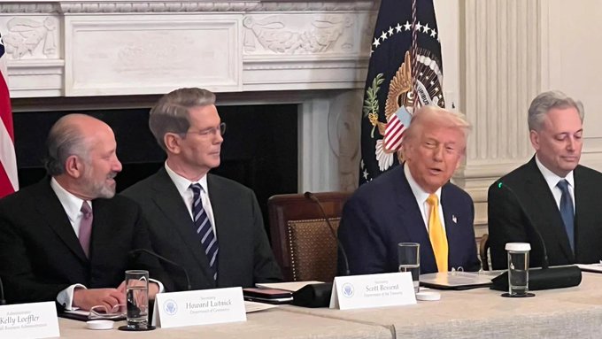 President Donald Trump seated at a White House cabinet table during a roundtable meeting, with a nameplate reading 'Scott Bessent, Secretary of the Treasury' visible in front of him, alongside other officials including one labeled 'Howard Lutnick.'