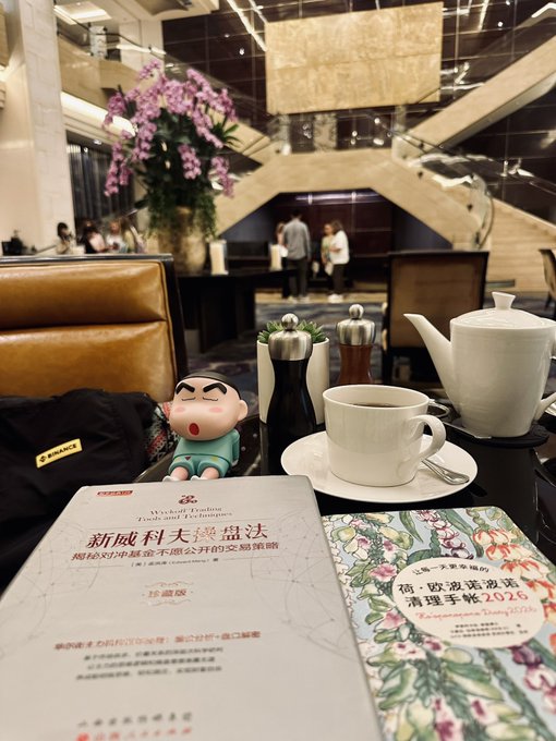 A hotel lobby scene features a table with books titled 'The Practice of the Wild' and Chinese titles about Taiwan, alongside a teapot, teacup, and a small Crayon Shin-chan figurine.