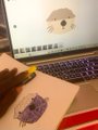 A photo of hands drawing pixel art on graph paper next to a laptop displaying a similar pixel art character, likely from a gaming context.