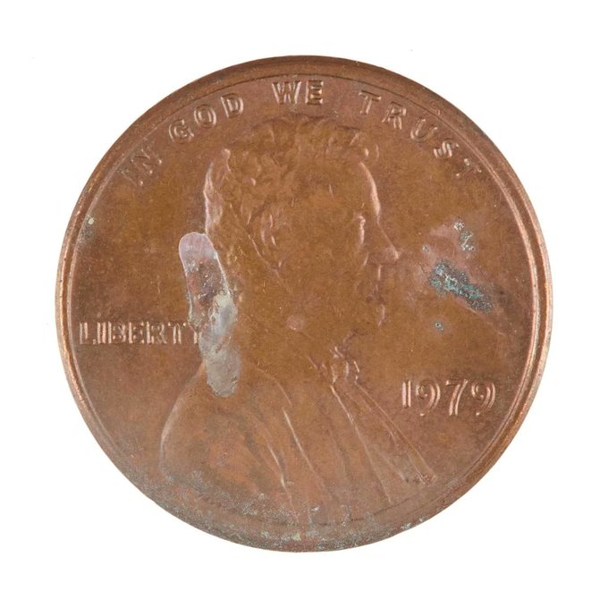A close-up of a worn 1979 US Lincoln penny showing 'IN GOD WE TRUST' and 'LIBERTY' with some discoloration on its surface.