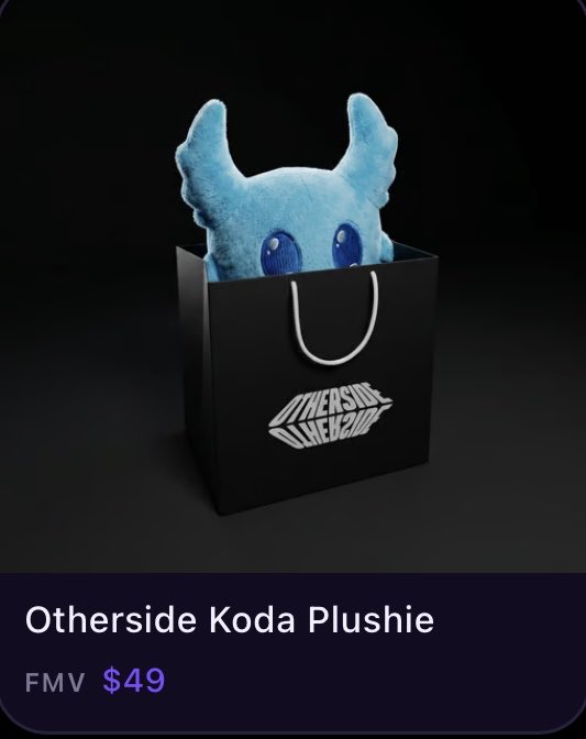 The image shows a blue plush toy doll placed inside a black paper bag with a white handle sitting against a black background. The image also includes text that appears to be an advertisement for the Koda plushie, likely featuring a photo of the toy as well.