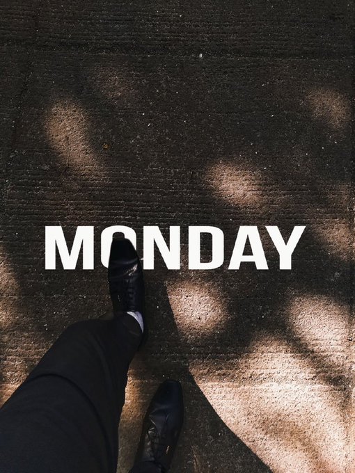 A first-person view shows feet in dark sneakers walking on a concrete surface, with the word 'MONDAY' stamped in large white letters on the ground.