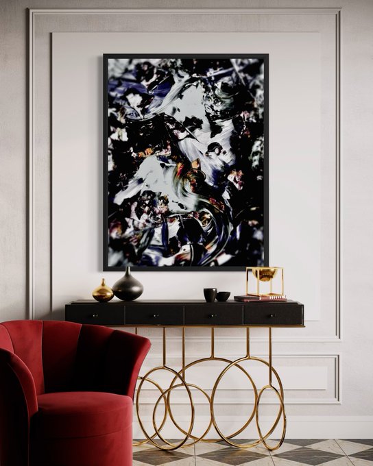 An elegant interior decor scene featuring an abstract black and white framed artwork mounted above a black and gold console table with a red velvet chair in the foreground.