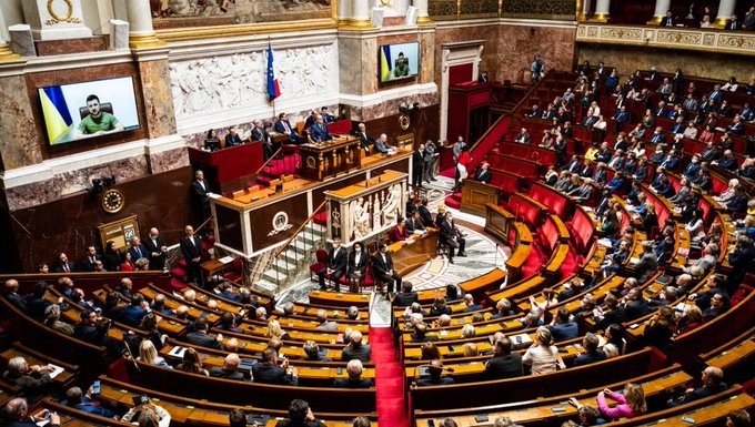 The image shows the National Assembly of France in session, with the EU flag and a large screen displaying a speaker, where lawmakers gathered to vote on amendment I-3898 (38 to 37) related to imposing crypto-to-stablecoin transactions under the flat tax starting January 1, 2027.