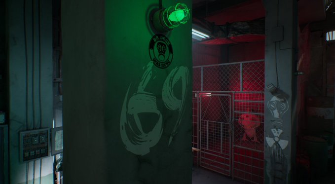 A dimly lit industrial or sci-fi scene features a green-lit pillar with a graffiti drawing of a figure wearing a gas mask, next to a chain-link fence enclosure lit with red light.