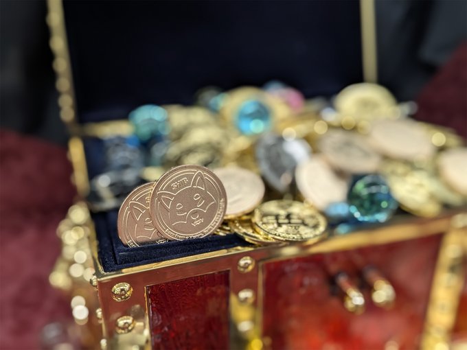A treasure chest overflowing with gold and silver coins features two cat-themed coins in the foreground, one bearing the year '2017'.