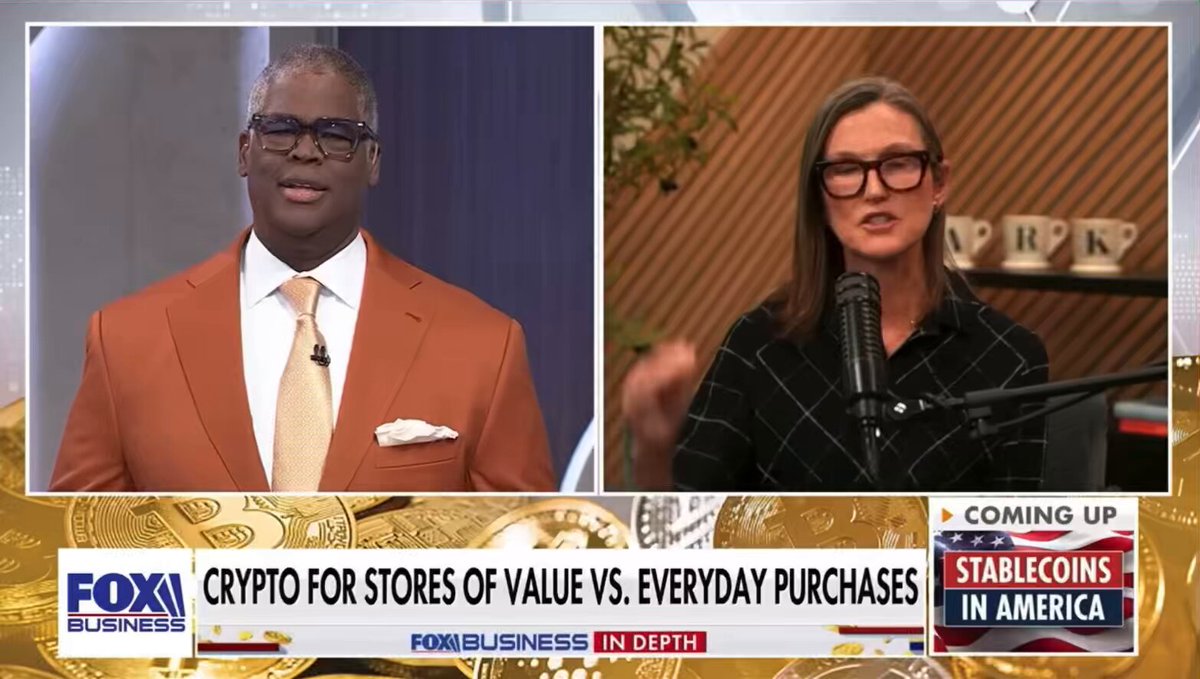 The image shows a man wearing an orange suit and tie, and a woman wearing glasses speaking into a microphone. They are both talking about Bitcoin and its value compared to everyday purchases. The background of the image features a gold banner with text that reads "CATHIE WOOD: 21 million units were up to 20 million that have been minted. Only one more million to go." There is also a text that says "bitcoin is mathematically metered. There will be no supply response. And right now the supply is increasing at 0.9% roughly per year which is lower than gold's long term." The image focuses on the conversation between the two individuals and their discussion about Bitcoin as an investment or currency.