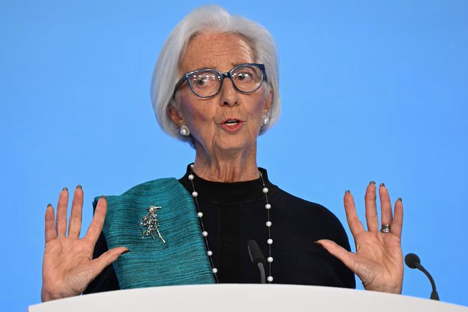The image features an older woman wearing glasses, a black sweater, and pearls, standing behind a podium with her hands outstretched as if she's giving a speech or presentation. The background of the image is blue, which contrasts nicely with the white podium where the woman stands. There are no texts visible in the image, but it appears to be an image related to Bitcoin regulation, as indicated by the caption provided.