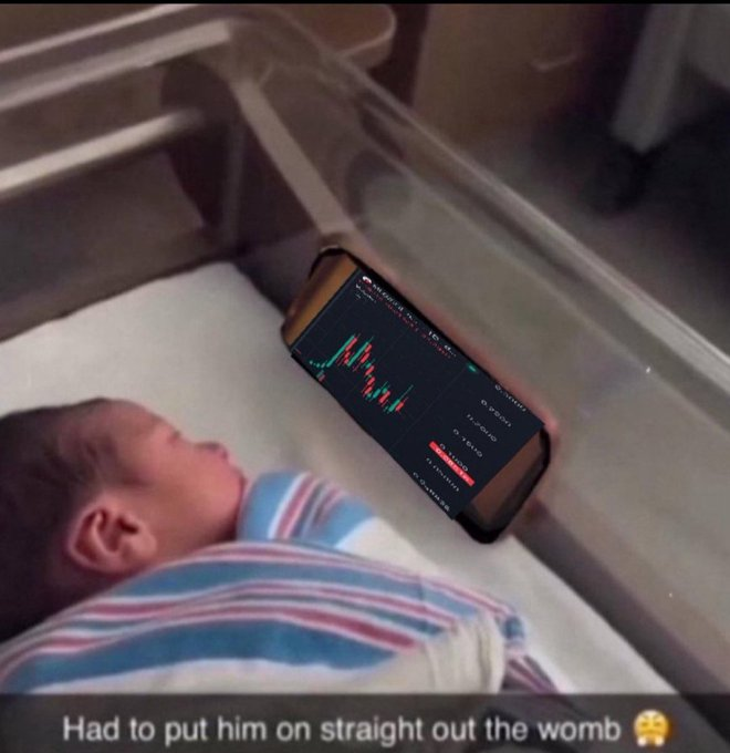 A newborn baby sleeps in a hospital crib beneath a smartphone displaying a stock trading chart, captioned 'Had to put him on straight out the womb 😳'.