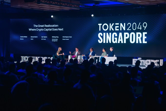 A panel discussion at TOKEN 2049 Singapore titled 'The Great Reallocation: Where Crypto Capital Goes Next' featuring speakers Jessica Walker (Botanic), Richard Byrnes, Dan Tapiero (DZKC), ShiXiang Tang (Mu Digital), and Chris Hurmer-Clark (Winter Muters), seated on a stage in front of an audience.