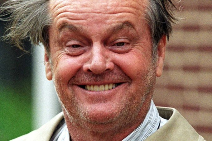 A close-up photograph shows actor Jack Nicholson smiling broadly, wearing a tan jacket and striped shirt.
