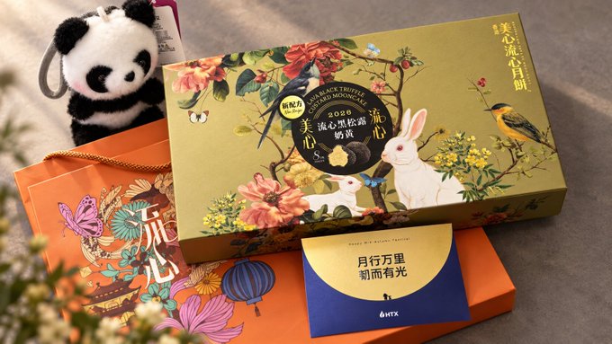 A festive gift box of Bird's Nest Black Trilogy with floral and rabbit designs, accompanied by a panda plush toy and an orange gift bag featuring traditional Chinese motifs, with an HTFX card reading '月行万里 前面有光'.